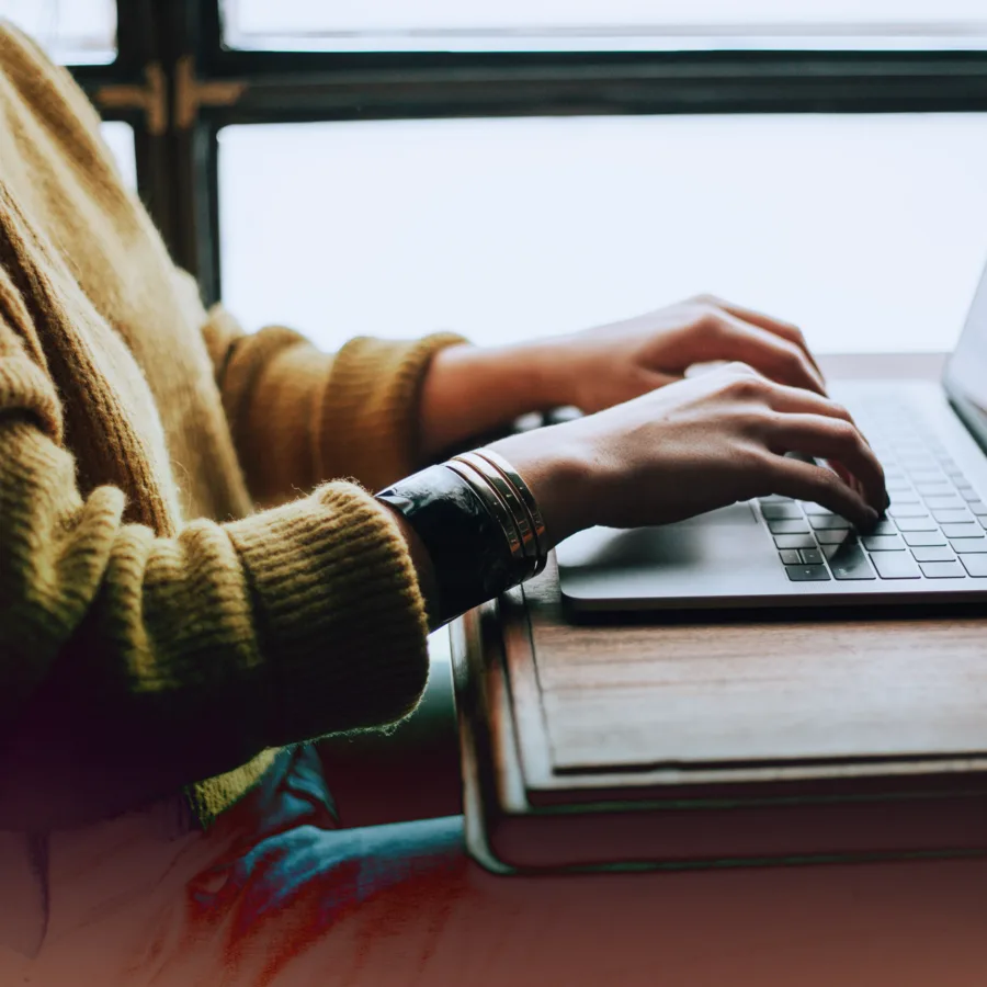 A person with a yellow sweater typing on a laptop.