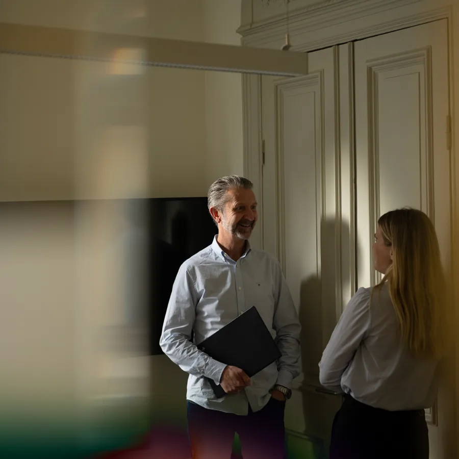 Two people standing in a meeting room with a blurred background.