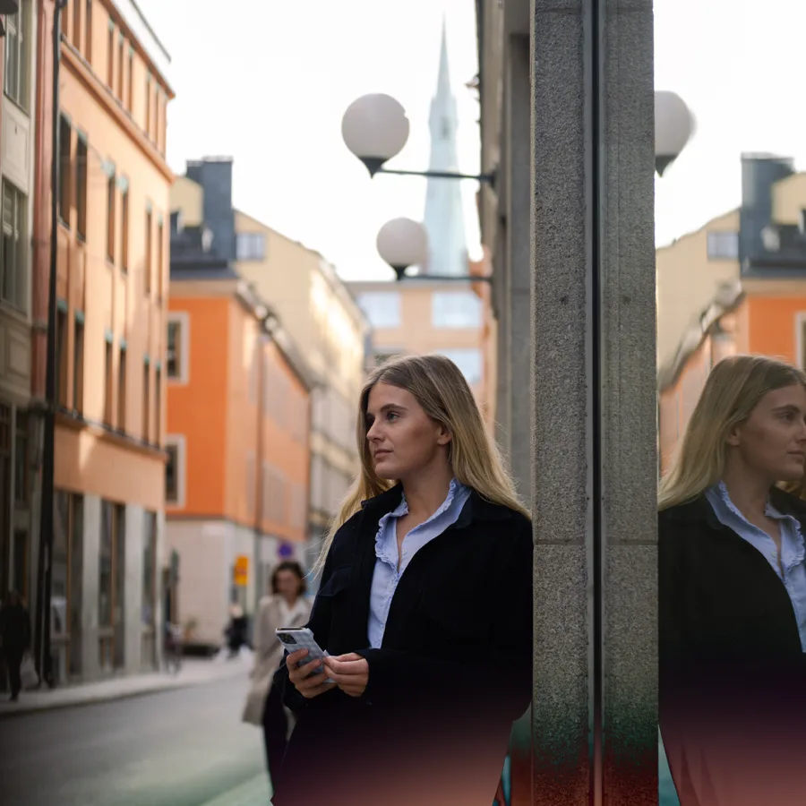 Street scene with buildings and a woman holding a phone, looking in the distance.