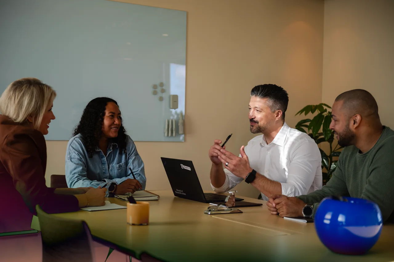 A modern office setting with a group of people seated around a wooden conference table.