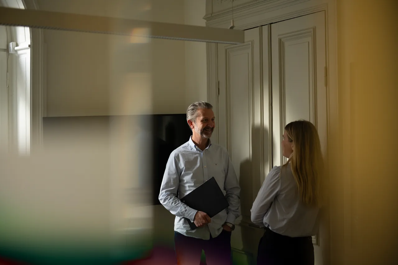 Two people standing in a meeting room with a blurred background.